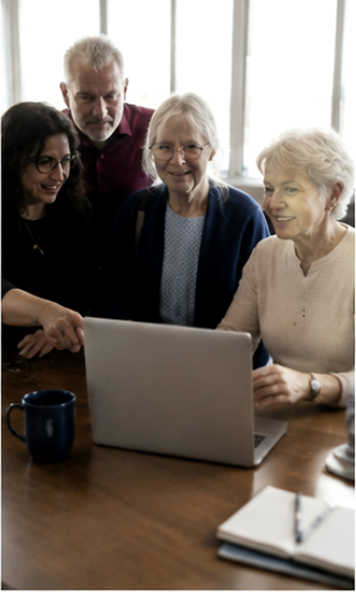 Four older adults smiling around a laptop at a table